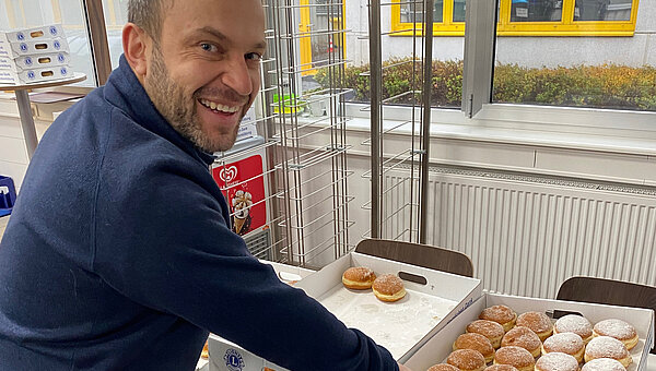 Ein lächelnder Mitarbeiter, der sich einen Krapfen nimmt.